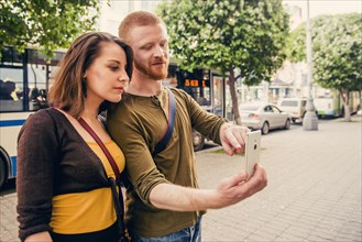 Caucasian couple using cell phone on city sidewalk