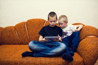 Caucasian brothers using digital tablet on sofa