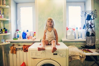 Caucasian girl sitting on washing machine