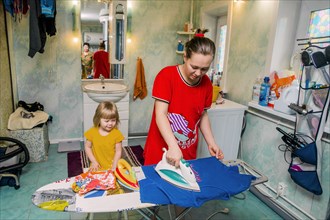 Caucasian mother and daughter ironing laundry