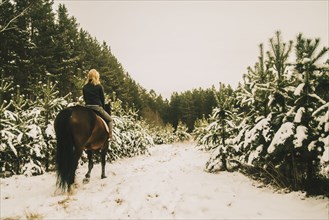 Caucasian woman riding horse on snowy path