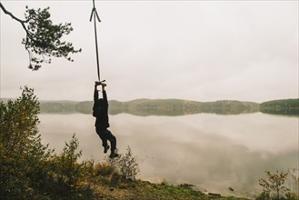 Man hanging on rope swing at remote lake