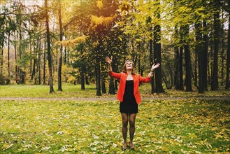 Caucasian woman tossing autumn leaves in park