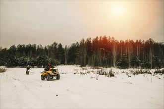 Caucasian men riding all-terrain vehicles in snowy forest
