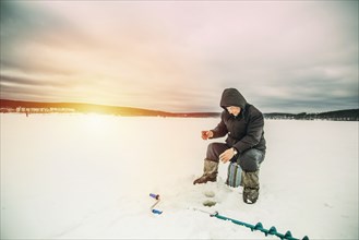 Man ice fishing in frozen lake