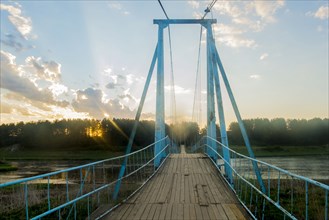 Sunbeams on wooden footbridge over river