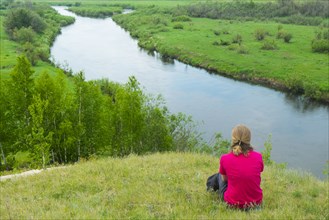Pensive woman sitting on hill at river