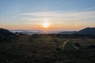 Camping tent in barren field at sunset