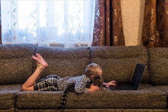 Caucasian boy laying on sofa with cat using laptop