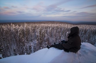 Caucasian man sitting in snow admiring scenic view of forest