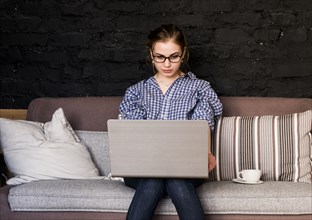 Caucasian woman sitting on sofa using laptop