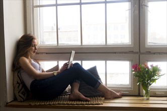 Caucasian woman sitting at window using digital tablet