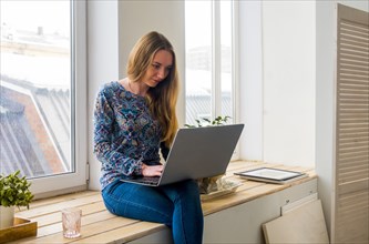 Caucasian woman sitting at window using laptop