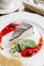 Cheesecake slice on plate with powdered sugar and berry sauce