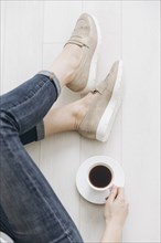 Legs of woman sitting on wooden floor drinking coffee