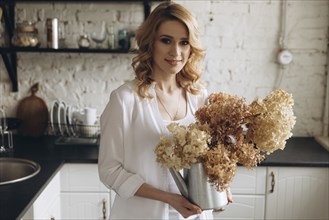Middle Eastern holding kettle of flowers in domestic kitchen