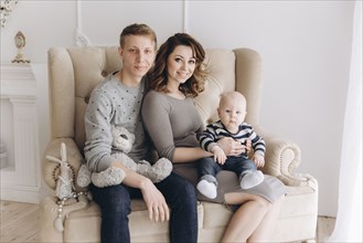 Portrait of Caucasian mother and father on love seat with baby son