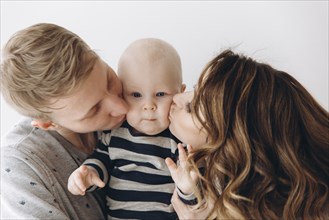 Caucasian mother and father kissing baby son on cheek