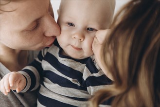 Caucasian mother and father kissing baby son on cheek