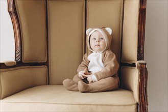 Caucasian baby boy sitting in armchair wearing bear costume