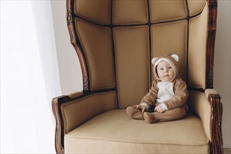 Caucasian baby boy sitting in armchair wearing bear costume