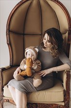 Caucasian mother sitting in armchair with baby son wearing bear costume