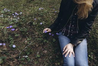 Woman sitting in grass picking purple flower