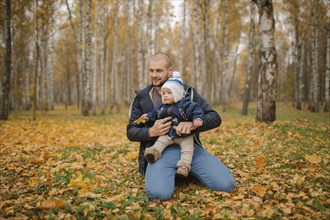 Middle Eastern father kneeling in park with baby son in autumn