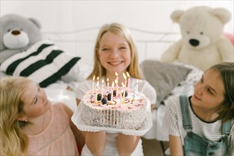 Smiling Middle Eastern sisters with birthday cake in bedroom