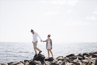 Middle Eastern couple walking on rocks near ocean