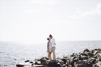 Middle Eastern couple hugging on rocks near ocean