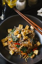 Chopsticks on bowl with noodles and tofu