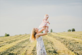 Mother lifting baby daughter in field