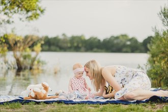 Mother and daughter playing with stuffed animals on blanket near lake