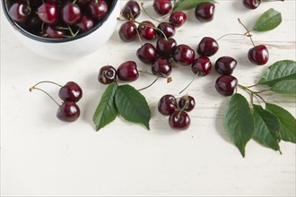 Cherries and bowl on white wooden table