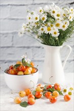 Cherries on white wooden table near vase of flowers