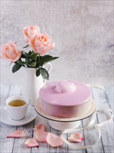 Pink cake with tea near vase of flowers