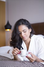 Hispanic woman drinking espresso on bed