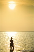 Silhouette of Mixed Race woman wading in ocean at sunset
