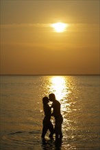 Silhouette of Caucasian couple kissing in ocean at sunset