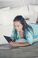Mixed Race girl laying on bed reading digital tablet