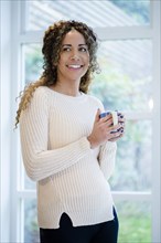 Woman standing near window holding coffee cup