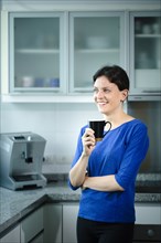 Smiling Caucasian woman drinking coffee in kitchen