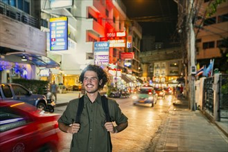 Smiling man carrying backpack in city at night
