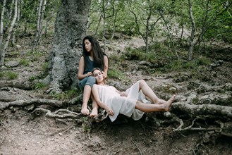 Women relaxing on tree roots in forest