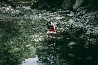 Caucasian woman crouching on rocks at pool of water