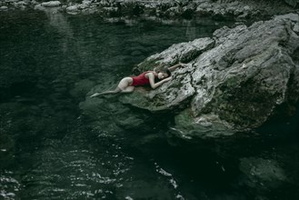 Caucasian woman laying on rocks in pool of water