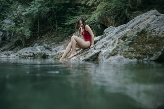 Caucasian woman sitting on rocks at pool of water