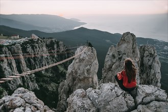 Caucasian woman sitting on mountain near footbridge