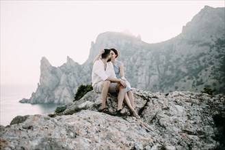 Caucasian couple sitting on rocks at lake